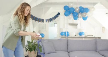 Kadın balonları ayarlıyor, çörekleri ve kap kekleri çatı katında doğum günü için kahve masasına koyuyor. Kutlama, şenlik, dekor, ortam, zarafet, rahatlık, iç mekan.