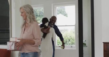 Paketlenmiş hediyeler, kıdemli kadın ve Afrika kökenli Amerikalı erkek ev sahibesinin rehberliğinde oturma odasında turluyor. Aile, kutlama, iç mekan, arkadaşlık, modern, sıcaklık, sosyal