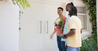 Eve vardıklarında, çeşitli arkadaşlar hediye kutusuyla beyaz ön kapıya gelip ev sahiplerini selamlıyorlar. Hoş geldin, misafirperverlik, dostluk, kutlama, açık hava, dekor, yeşillik