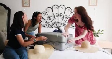 Çeşitli bayan arkadaşlar bavullarını yataklarında açıyor, tabletten seyahat planlarını kontrol etmeden önce şapkalarını ayırıyorlar. Macera, seyahat, arkadaşlık, eğlence, yaşam tarzı, hayat dolu, neşeli