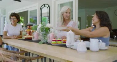 Çeşitli kadınlar tabak alıyor ve ev verandasındaki gelin partisinde minyatür pasta seçiyorlar. Kutlama, dostluk, zarafet, aşçılık, bahar, neşe, eğlence