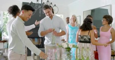 Oturma odasının etrafında toplanan arkadaşları kutlamak için flütle köpüklü şarap açan bir adam. Kutlama, sosyalleşme, lüks, atmosfer, neşe, zarafet, çeşitlilik