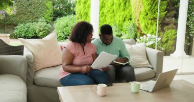 Veranda kanepesinde dizüstü bilgisayarı ve kahve fincanlarıyla sarılan çift. Romantizm, rahatlama, yaşam tarzı, teknoloji, boş zaman, bağ.