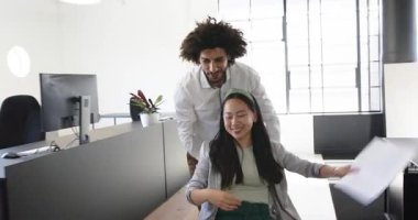 Mutlu meslektaşlar ofiste eğleniyor, erkekler modern ofiste kadınları ofis sandalyesine oturtuyor. İş, iletişim, iş, ofis çalışma ortamı kavramı.