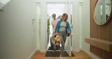 Çift eve bavullarıyla geliyor, seyahatten sonra rahatlamış ve mutlu görünüyorlar. Eve dönüş, varış, rahatlama, yolculuk