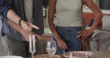 Çeşitli arkadaşlar, sarılmadan önce yemek masasını gösterip tabakları incelerken pano kullanıyorlar. Sosyal toplanma, uysallık, ev içi, çağdaş tasarım, arkadaşlık, iletişim, gündelik tarz