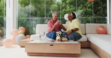 60. doğum gününü evde, tahta masanın yanında pasta ve işaretle kutlayan kıdemli arkadaşlar. Doğum günü, kutlama, dostluk, konfor, şenlik, dekor, neşe