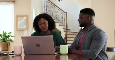 Afro-Amerikalı çift evde dizüstü bilgisayar kullanıyor, kahve içerken belgeleri tartışıyorlar. Yaşam tarzı, finans, teknoloji, iletişim, takım çalışması, planlama