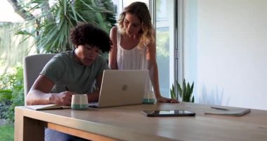 Evde dizüstü bilgisayarda çalışan genç bir çift. Etrafı yeşilliklerle çevrili. İşbirliği, takım çalışması, uzaktan çalışma, teknoloji, bitkiler, yaşam tarzı