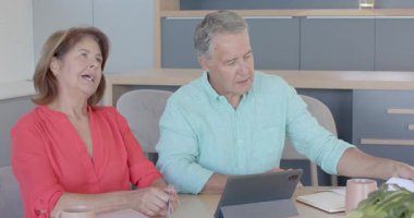 Mutfakta tablet kullanarak kredi kartı tutan yaşlı çift tost kupalarını geren faturaları inceliyor. Aile, yerli, iletişim, teknoloji, rahatlama, uyum, yaşam tarzı