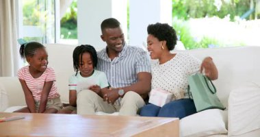 Parlak yaşam evindeki rahat beyaz koltukta oturan aile ellerinde akıllı telefon ve yeşil çanta tutuyorlar. Sıcaklık, sıcaklık, birliktelik, rahatlama, ebeveynlik, doğal ışık, neşe, aile zamanı, yeşillik.