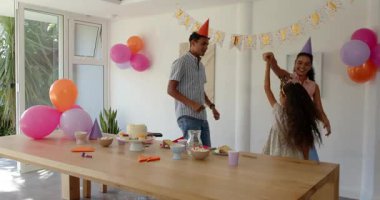 Evde, süslü parti mekanında çeşitli aileler doğum günü pastası ve konfetisinin tadını çıkarıyor. Kutlama, aile, neşe, dekorasyon, toplanma, tatlılar, şenlikler, aydınlık