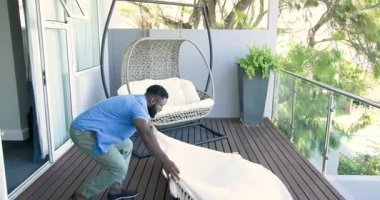 Afro-Amerikalı adam balkondan çıkıyor, battaniye seriyor, fotokopi çekiyor. Açık hava, boş zaman, yaşam tarzı, çağdaş, rahatlama, doğa, tasarım