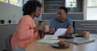 Genç çift mutfaktaki masada tablet ve dizüstü bilgisayarla belgeleri tartışıyor. İşbirliği, yerli, teknoloji, evrak, ev, yaşam tarzı