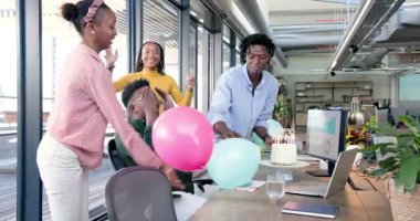 Afrikalı Amerikalı meslektaşlar ofis ortamında doğum gününü kutluyor, laptopla pastanın tadını çıkarıyorlar. Kutlama, takım çalışması, neşe, heyecan, ofis, toplantı, iş arkadaşları