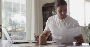 Tişört giyen, evde dizüstü bilgisayarla ders çalışan, incelenmek üzere notlar yazan bir adam açıyorum. Çalışma alanı, çalışma alanı, modern, profesyonel, konsantrasyon, üretkenlik, iç mekan