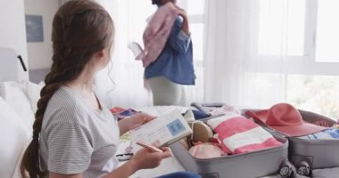 Afro-Amerikalı bir kadın, elinde tablet ve liste bulunan açık bavul hazırlıyor. Kopya alanı. Paketleme, seyahat, organizasyon, arkadaşlık, yaşam tarzı, yatak odası, macera, hazırlık