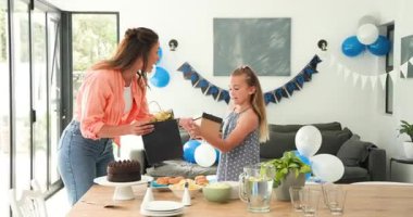 Anne ve kızı, hediye üstüne hediye olarak pasta ve balonlarla birlikte masada parti düzenliyor. Kutlama, aile, mutluluk, sevinç, bağlılık, şenlik, sıcaklık