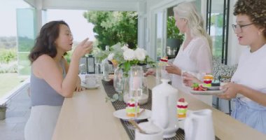 Çeşitli bayan arkadaşlar, üst düzey tabak yerleştirme ve kucaklaşmadan sonra terasta katmanlı kek yiyorlar. Toplanma, kutlama, zarafet, çeşitlilik, arkadaşlık, rahatlık, sükunet