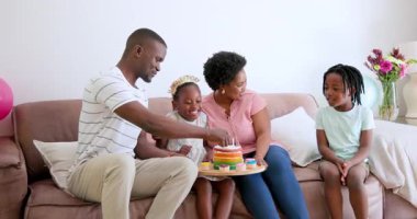 Afro-Amerikalı bir aile, doğum gününü kahverengi kanepede kutluyor ve bayram pastasının tadını çıkarıyor. Kutlama, doğum günü, konfor, birliktelik, neşe, dekor, pasta, aile