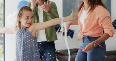 Üç kişilik aile doğum günü kutlaması için oturma odasında doğum günü afişleriyle sarılıp kurdele atıyor. Kutlama, neşe, birliktelik, şenlik, mutluluk, yerli, canlı