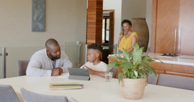 Anne telefonda konuşurken, baba oğluna tablet ödevinde yardım ediyor. Ebeveynlik, teknoloji, aile, çoklu görev, eğitim, iletişim