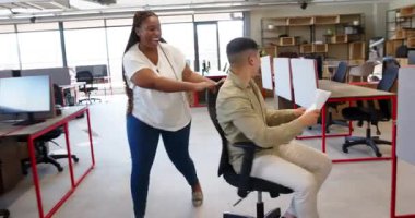 Afrika kökenli Amerikalı kadın çeşitli erkekleri bilgisayar ve malzemeler arasında döner sandalyeye oturtuyor. Ofis, işbirliği, üretkenlik, çalışma alanı, modern, parlak, takım çalışması