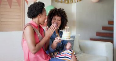 Pastayı mumlarla tutarken, Afrikalı Amerikalı kadınlar evde neşeyle doğum günü kutluyor. Kutlama, mutluluk, çeşitlilik, arkadaşlık