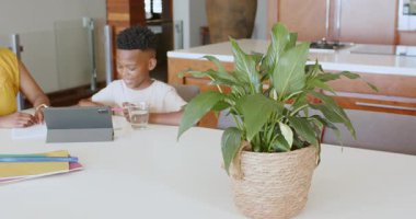 Anne oğluna mutfak masasında ödevlerinde yardım ediyor, tablet ve not defteri kullanıyor, evde. Ebeveynlik, teknoloji, eğitim, öğrenme, aile, öğretim