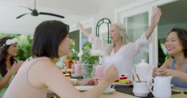 Müstakbel anne ve kız gelin arkadaşlarıyla çay içip düğün için terasta kek yiyorlar. Kutlama, dostluk, zarafet, kadınlık, rahatlık, neşe, samimiyet.