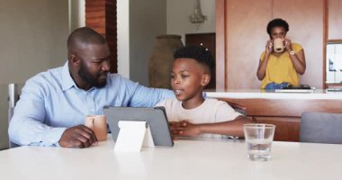 Anne mutfakta telefonla konuşurken baba ve oğul tablet kullanıyor. Aile, teknoloji, iletişim, ebeveynlik, çoklu görev, çocukluk