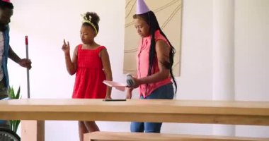 Afro-Amerikan ailesi evi süpürüyor, sonra baba sürpriz parti şapkasını çekip anneyi işaret ediyor. Aile, takım çalışması, kutlama, aile içi, bağ, neşe, gündelik