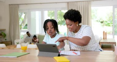 Afro-Amerikan ailesi tablet ve renkli kalemler kullanarak birlikte yemek masasında öğreniyorlar. Eğitim, takım çalışması, yaratıcılık, aile, etkileşim, aktivite, parlak, hayat dolu