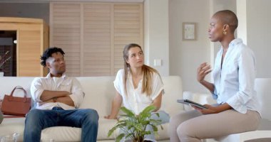 Afro-Amerikalı kadın elinde tabletle evdeki kanepede arkadaşlarıyla tartışıyor. Teknoloji, iletişim, arkadaşlık, eğlence, çeşitlilik, tartışma