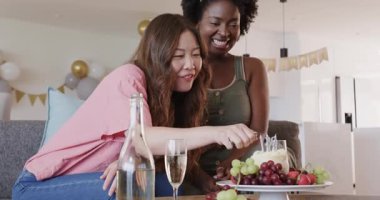 Afrikalı Amerikalı arkadaş gülüyor, Asyalı arkadaş pasta ve içeceklerle el çırpıyor. Kutlama, kahkaha, arkadaşlık, kilometre taşı, neşe, parti, şenlik