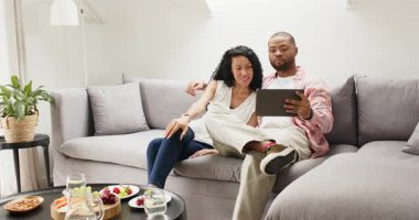 Tablet tebligatı çeşitli çiftlerin beyaz perdeye dokunmasını, gri kanepede gülücüklerini paylaşmalarını sağlar. Aile, rahatlama, teknoloji, konfor, samimiyet, modern, yaşam tarzı