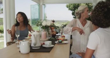 Çeşitli bayan arkadaşlar arkadaşlarıyla selamlaşıyor ve terasta çay ve mini keklerle kutluyorlar. Dostluk, toplanma, kutlama, açık hava, zarafet, ahenk, neşe