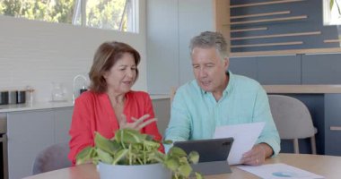 Tabletin sunduğu çeşitli üst düzey çiftler mutfak masasında mali durumu analiz ediyorlar. İşbirliği, tartışma, teknoloji, danışma, üretkenlik, modernlik, katılım