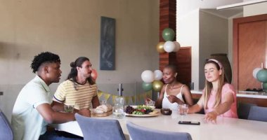 Partide, arkadaşlar birlikte yemek yiyor, gülümsüyor ve yemek masasında selfie çekiyorlar. Arkadaşlık, toplanma, akıllı telefon, mutluluk, yemek, sosyalleşme