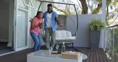 Afrika kökenli Amerikalı çift balkonda yıldönümü kutlaması yapıyor. Hediye kutusu ve meyve tutuyorlar. Kutlama, balkon, mutluluk, romantizm, hediye, yaşam tarzı, açık hava, samimiyet