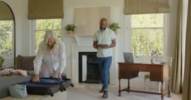 Tabletteki seyahat planlarını onayladıktan sonra çeşitli yaşlı çiftler oturma odasında bavullarını hazırlıyorlar. Seyahat, paketleme, organizasyon, planlama, yerli, ev, yaşam tarzı