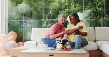 60. yaş gününü sıcak ev bölgesinde pasta ve sürahiyle kutlayan kıdemli arkadaşlar. Kutlama, dostluk, neşe, konfor, toplanma, şenlik, kahkaha, sıcaklık