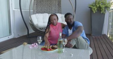 Afrika kökenli Amerikalı çift balkonda yıldönümlerini kutluyor, tatlıyla şarabın tadını çıkarıyorlar. Romantizm, kutlama, samimiyet, açık hava, şarap, ortaklık, neşe, yeşillik