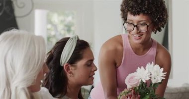 Çeşitli bayan arkadaşlar kanepede gülüyorlar. Renkli bir buketle gelen arkadaşlardan sonra sarılıyorlar. Arkadaşlık, neşe, sıcaklık, samimiyet, bağlantılar, kutlamalar, köylülük