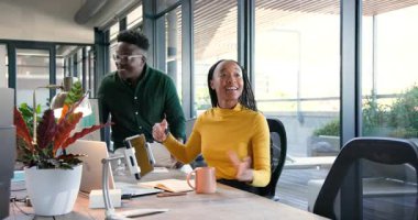 Afrikalı Amerikalı meslektaşlar modern ofiste başarıyı kutluyorlar, dizüstü bilgisayar ve tablet kullanarak. Takım çalışması, işbirliği, beşlik çakma, beyin fırtınası, motivasyon, verimlilik, başarı