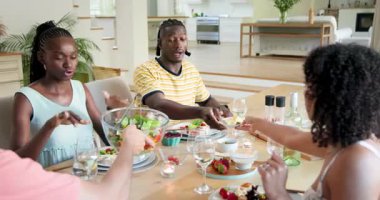 Modern evdeki çeşitli arkadaşlar yemek masasında oturup salata dağıtıp sohbet ediyorlar. Toplanma, yemek, mutfak, arkadaşlık, rahatlama, modern sohbet