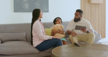 Çeşitli aileler rahat oturma odasında, tablet ve pelüş oyuncaklar kullanarak mutlu haberler veriyorlar. Duyuru, aile, rahatlık, ilişki, neşe, birliktelik, ebeveynlik, kutlama