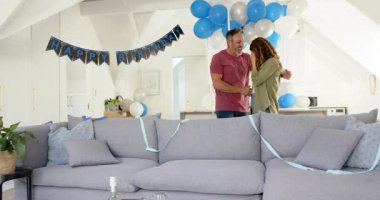 Mutlu yıllar pankartı ve balonlar altında dönen ve sarılan bir çift. Kutlama, romantizm, konfor, şenlik, neşe, dekor, birliktelik