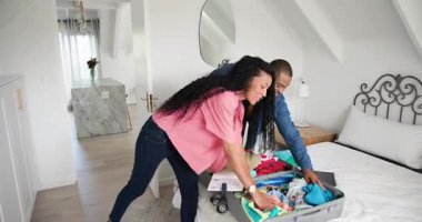 Yatakta tekerlekli bavulu açtıktan sonra, çeşitli çiftler giysileri katlıyor ve gezi için tableti gözden geçiriyorlar. Macera, paketleme, seyahat, organizasyon, samimi, genç, yaşam tarzı