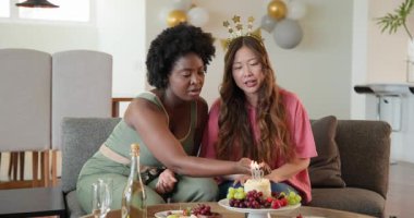 Afro-Amerikalı, Asyalı arkadaşlar 30. doğum gününü oturma odasında kutluyorlar, pasta ve şampanya paylaşıyorlar. Kutlama, doğum günü, arkadaşlık, toplantı, parti, neşe, şenlik